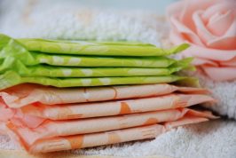 Featured Image Research Spotlight Menstrual Inequity: Image description a pile of sanitary towels of different colours on a white towel and a pink rose to the right