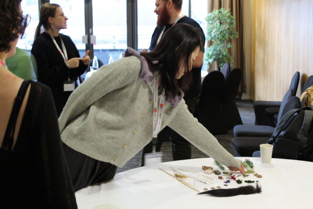 A girl picking up a leaf from a selection of feathers, twigs, leaves and other miscellanious items. This was done as part of the workshop held by camille straatman.